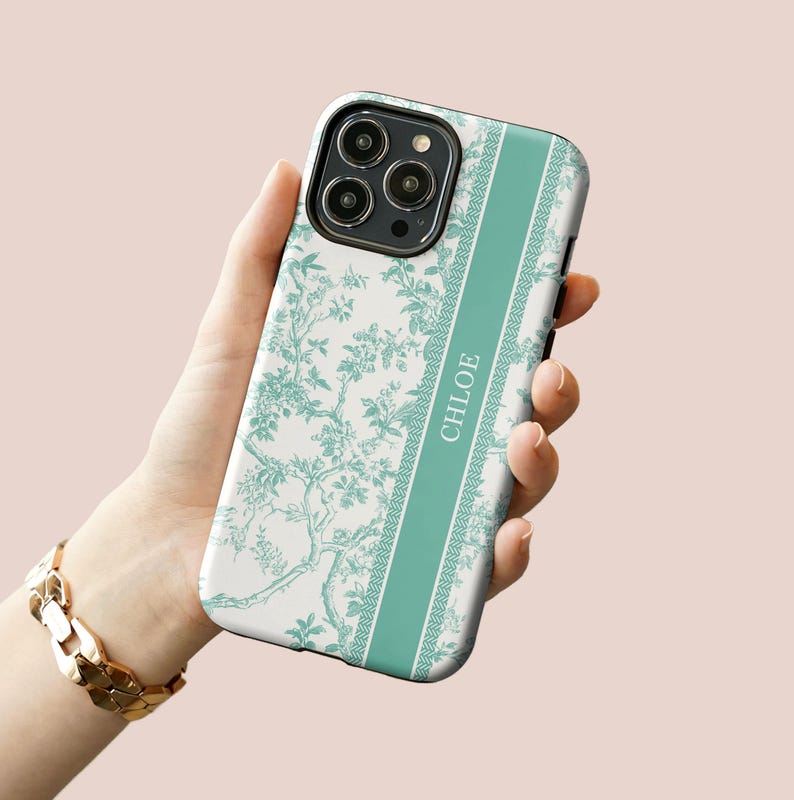May include: A white phone case with a green floral pattern and a green stripe down the side. The stripe has the name "CHLOE" written on it.