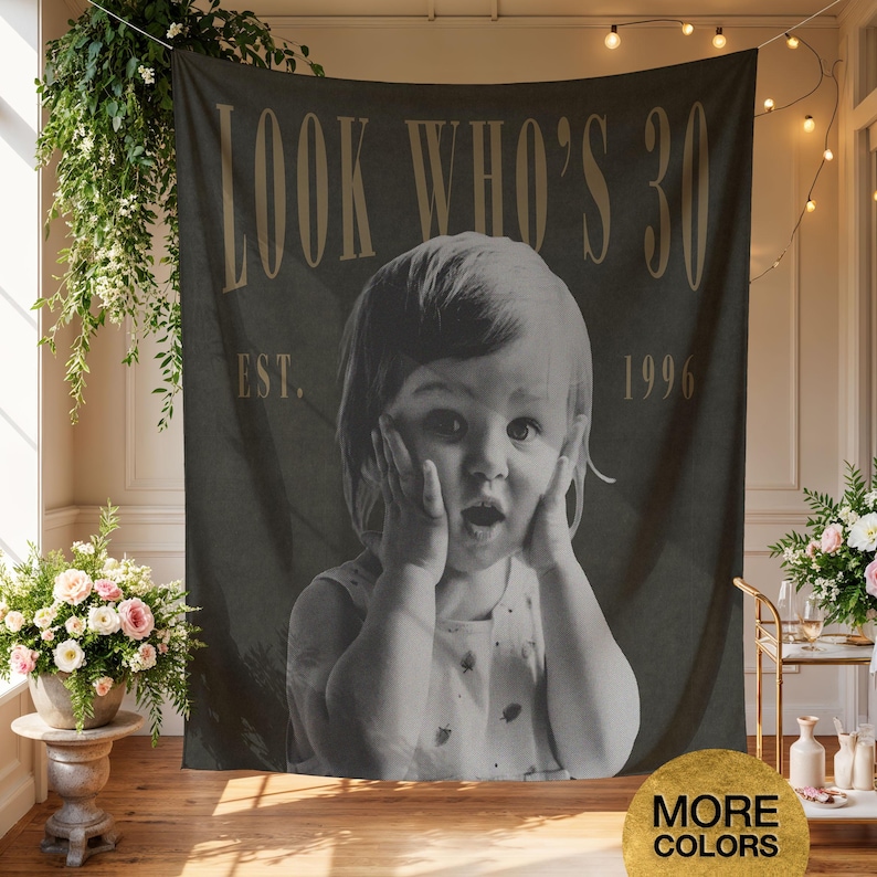 May include: A dark gray rectangular wall tapestry featuring a black and white photograph of a child with hands on their cheeks. The text reads LOOK WHO'S 30 at the top and EST. 1996 at the sides in a gold serif font. The fabric hangs vertically.