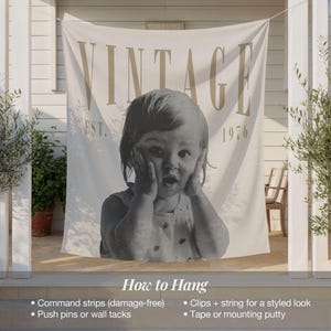 May include: A cream-colored fabric wall hanging featuring the word VINTAGE in large tan letters at the top, the text EST. 1976, and a large black and white photograph of a child with hands on their cheeks. The bottom includes hanging instructions.
