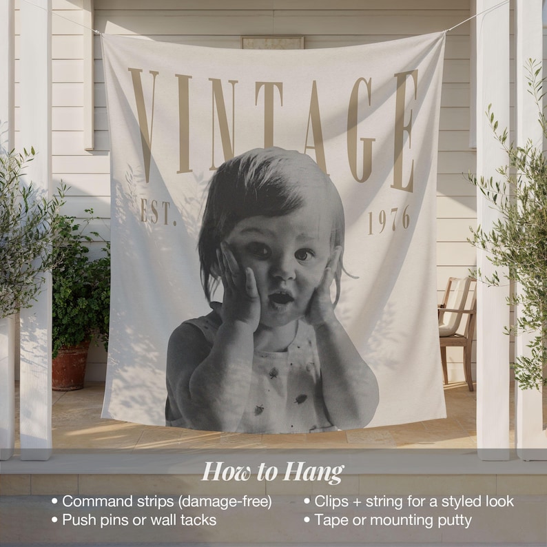 May include: A cream-colored fabric wall hanging featuring the word VINTAGE in large tan letters at the top, the text EST. 1976, and a large black and white photograph of a child with hands on their cheeks. The bottom includes hanging instructions.