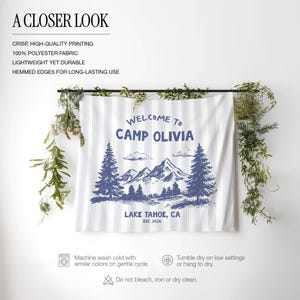 May include: A white and blue striped fabric banner with the text "WELCOME TO CAMP OLIVIA LAKE TAHOE, CA EST. 2026" and a mountain and pine tree graphic. The banner is made of 100% polyester fabric.