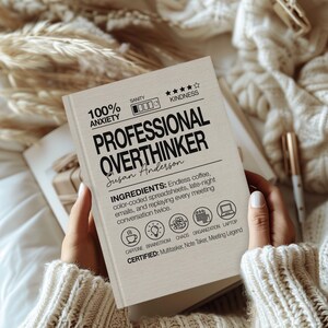 May include: A book titled "PROFESSIONAL OVERTHINKER" with the author's name, Susan Anderson, printed on the cover. The cover also includes the text "100% ANXIETY" and "INGREDIENTS: Endless coffee, color-coded spreadsheets, late-night emails, and replaying every meeting conversation twice."