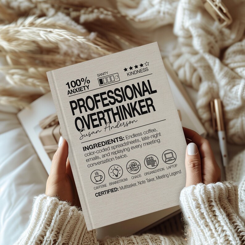 May include: A book titled "PROFESSIONAL OVERTHINKER" with the author's name, Susan Anderson, printed on the cover. The cover also includes the text "100% ANXIETY" and "INGREDIENTS: Endless coffee, color-coded spreadsheets, late-night emails, and replaying every meeting conversation twice."