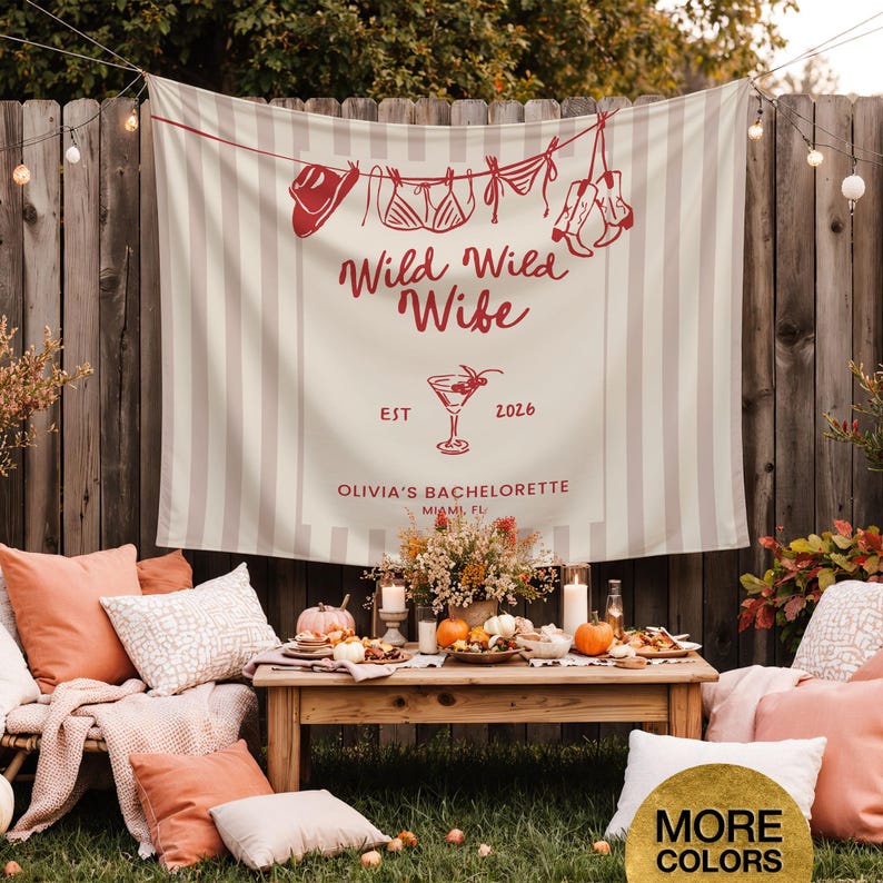 Puede incluir: Una pancarta a rayas beige y blancas con el texto "Wild Wild Wife" y "Olivia's Bachelorette Miami, FL" en rojo. La pancarta tiene ilustraciones de un sombrero de vaquero, lencer&iacute;a y botas. Una mesa de madera est&aacute; puesta con calabazas, flores y comida.