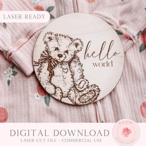 Peut inclure: Un panneau rond en bois avec un ours en peluche gravé au laser et les mots "hello world". Le panneau est brun clair et repose sur un body rose à motifs floraux. Le panneau est un téléchargement numérique.