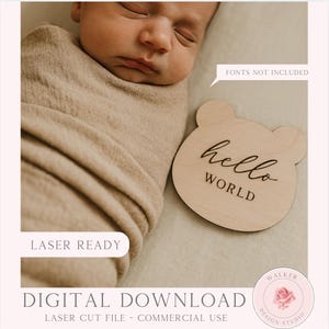 Può includere: Un neonato addormentato avvolto in una coperta beige accanto a un cartello di legno a forma di orso. Il cartello recita "hello WORLD" in un carattere scritto a mano. L'immagine include anche il testo "LASER READY" e "DIGITAL DOWNLOAD".