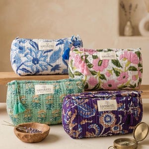 Può includere: Quattro trousse per cosmetici trapuntate con motivi floreali blu, rosa, verdi e viola. Ogni borsa ha un nappa abbinata e un'etichetta che dice "sanskriti en provence". Sono visibili anche una ciotola di legno con lavanda e una bussola.