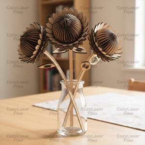 Può includere: Un vaso di vetro trasparente contiene tre sculture di girasoli in legno. I girasoli hanno petali a strati e centri dettagliati. Anche gli steli e le foglie sono in legno. Il testo "CozyLaser Files" è stampato sull'immagine.