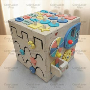 May include: A wooden activity cube with various colorful shapes, numbers, and interactive elements. The cube features a lock, gears, and a spinning wheel. The text "Cozy Laser Files" is printed on the cube.