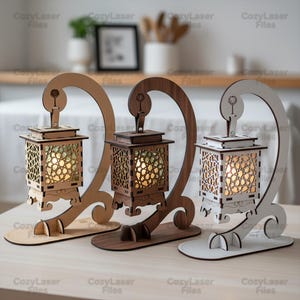 以下が含まれることがあります： 精巧な切り絵模様が施された3つの木製ランタン。それぞれ温かみのある光を内包しています。ベージュ、ブラウン、白の曲線的な木製スタンドで支えられています。各ランタンのベースは平らな長方形です。