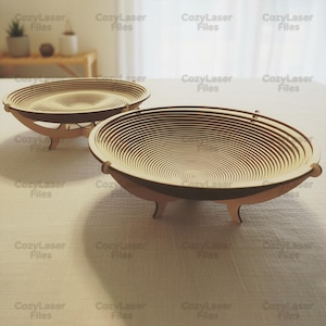 Może przedstawiać: Dwie drewniane misy dekoracyjne ze spiralnym wzorem. Misy są jasnobrązowe i mają warstwową konstrukcję. Każda misa jest podparta przez trzy małe nóżki. Tekst "CozyLaser Files" jest widoczny.