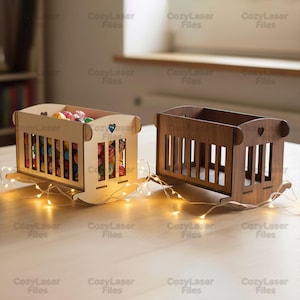 May include: Two miniature wooden rocking cribs, one in a light natural wood finish and one in a dark brown wood finish. Each crib features vertical slats, a small heart-shaped cutout on the headboard, and curved rockers at the base.