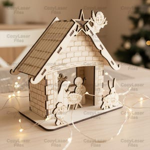 May include: A laser-cut wooden nativity scene featuring a pitched roof, brick-effect walls, and figures of Mary, Joseph, baby Jesus, a lamb, and a rabbit. An angel and star decorate the roof. The image includes the text "CozyLaser Files".