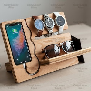 May include: Wooden charging station with slots for a smartphone, three watches, and sunglasses. The phone is charging. The station is made of light-colored wood and has the text "Cozy Laser Files" repeated on it.