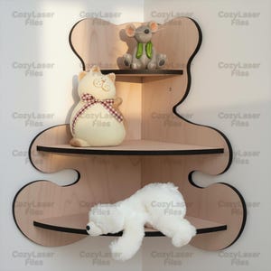 May include: A wooden corner shelf in the shape of a bear, with three shelves. The shelves hold a stuffed cat with a bow, a gray mouse with a green scarf, and a white plush polar bear. The shelf is made of light-colored wood with black trim.
