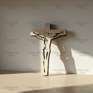 May include: A wooden crucifix depicting Jesus Christ, with a detailed cutout design. The cross is crafted from light-coloured wood with a dark border, creating a shadow on the wall. The image is well-lit, showcasing the intricate details.