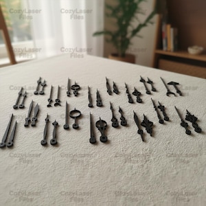 May include: A collection of black clock hands in various designs, including straight, curved, and ornate styles. The hands are arranged on a neutral-colored surface, with the text "CozyLaser Files" visible in the background.