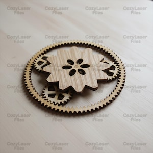 May include: A set of wooden gears, laser-cut from light-coloured wood. The design features a large gear with a flower-shaped centre, surrounded by smaller gears. The text "CozyLaser Files" is repeated around the image.