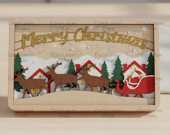 May include: A wooden Christmas-themed shadow box with a layered design. It features reindeer pulling a sleigh with Santa, houses, trees, and the text "Merry Christmas" in gold glitter. The frame is light brown.