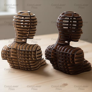 Może przedstawiać: Dwie drewniane rzeźby popiersi, jedna jasna i jedna ciemna, są wystawione na drewnianej powierzchni. Rzeźby są zbudowane z warstwowych kawałków drewna, tworząc efekt trójwymiarowy. Tekst "CozyLaser Files" jest widoczny w tle.