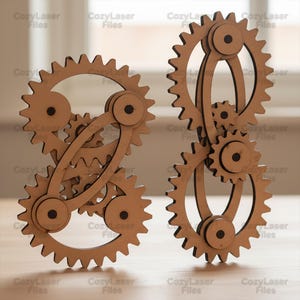 May include: Two wooden gear sculptures with interlocking designs. The gears are made of light brown wood and feature intricate cut-out details. The text "CozyLaser Files" is visible in the background. These decorative pieces could be used as home decor.