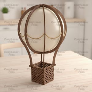 May include: A decorative hot air balloon model constructed from dark brown wood with a lattice-patterned square basket base. The balloon section features a smooth, off-white spherical centre framed by curved wooden ribs and thin beige rope accents.