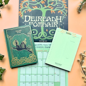 May include: An assortment of stationery items, including a 2026 diary, a calendar, and a notepad. The diary and calendar feature Celtic knot designs and the words "Deireadh Fómhair." The color palette includes green, gold, and black.