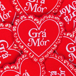 May include: A close-up of several red felt heart-shaped patches with white embroidered lettering that reads "Gr&aacute; M&oacute;r".