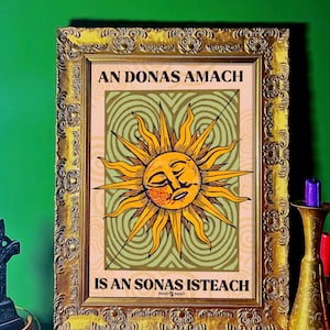 以下が含まれることがあります： 金色の装飾フレームに入ったプリント。プリントには、顔と光線を持つ様式化された黄色の太陽が、緑とベージュの背景に描かれています。「AN DONAS AMACH IS AN SONAS ISTEACH」というテキストが表示されています。