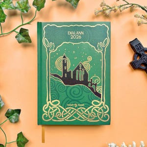 May include: A green 2026 journal with gold accents and the text "DIALANN" and "FADO FADO". The cover features a silhouette of a building and Celtic knot designs. A gold ribbon bookmark is visible.