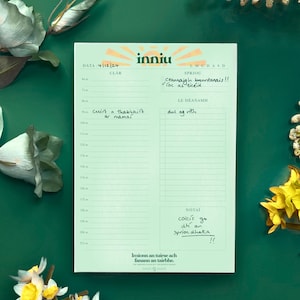 Könnte beinhalten: Ein hellgrüner Tagesplaner mit dem Wort "inniu" oben. Der Planer hat Abschnitte für Datum, Zeitplan und Notizen. Der Planer ist von weißen und gelben Blumen auf einem grünen Hintergrund umgeben.