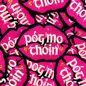 May include: Pink fabric patches with the text "p&oacute;g mo choin" in white lettering. The patches are shaped like lips and have a black outline.