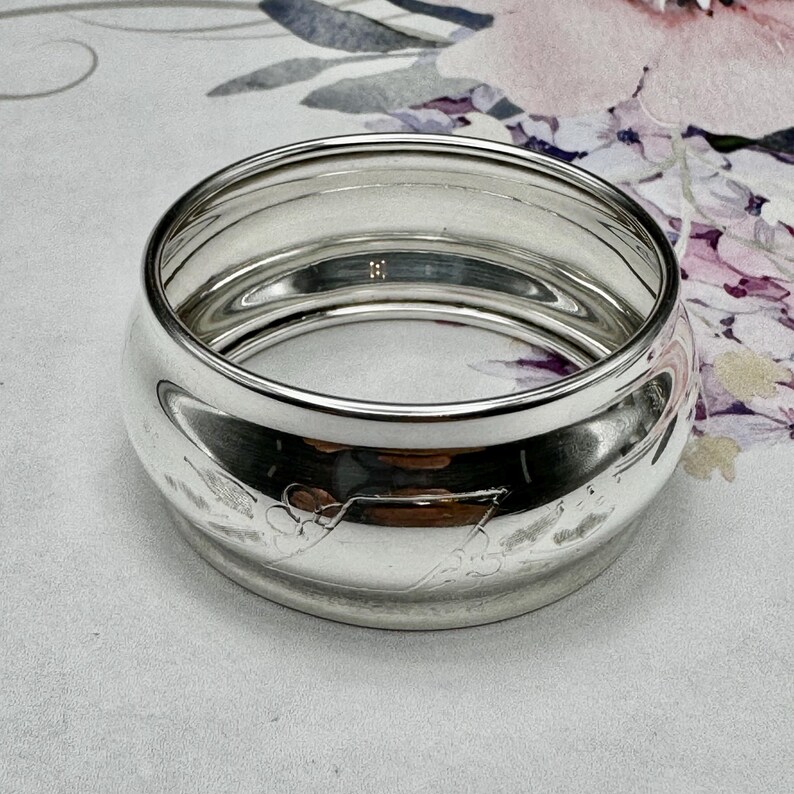 Op de afbeelding: Zilveren servetring met een decoratief ontwerp. De ring is rond en heeft een gladde, gepolijste afwerking.