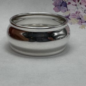 Op de afbeelding: Een zilveren servetring met een afgerond, licht uitlopend ontwerp. De ring is gepolijst en reflecteert licht.