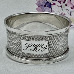 May include: Silver napkin ring with a wavy pattern and an engraved inscription that reads "P.K.C."