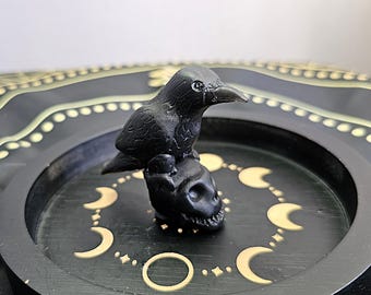 May include: Black crow figurine perched atop a black skull, both sitting on a black tray with gold crescent moon designs.
