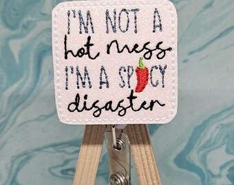 May include: White glitter badge holder with a red chili pepper and the text "I'm not a hot mess I'm a spicy disaster".