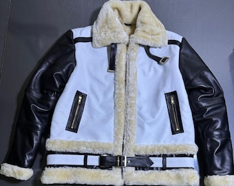 May include: A white and black jacket featuring a thick cream-colored faux fur lining on the collar, cuffs, and hem. The jacket includes black sleeves, two vertical zippered pockets with gold hardware, and a black buckled belt at the waist.