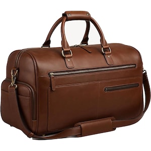 Könnte beinhalten: Eine braune Leder-Duffel-Tasche mit einem oberen Griff und einem abnehmbaren Schultergurt. Die Tasche hat mehrere Reißverschlussfächer und goldfarbene Hardware. Die Tasche ist für Reisen konzipiert und hat einen klassischen, raffinierten Look.