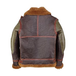 May include: A brown leather jacket with a shearling collar and trim. The jacket features olive green sleeves and red stitching details. The back view showcases the jacket's design and construction, highlighting its vintage style.