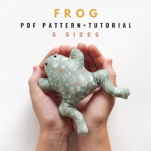 Könnte beinhalten: Ein salbeigrünes Stofffrosch-Spielzeug mit einem weißen botanischen Muster aus Monden und Sternen. Der Text darüber lautet FROG PDF PATTERN+TUTORIAL 5 SIZES. Der Frosch hat einen runden Körper, vier Gliedmaßen und kleine dunkle Augen.