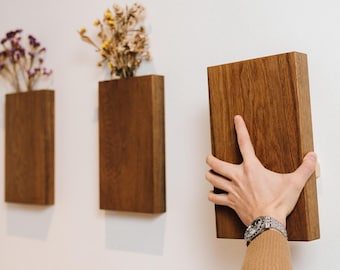 May include: Three wooden wall mounted planters with dried flowers. A person is holding a fourth planter to add to the wall.