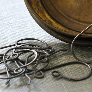 Puede incluir: Un montón de aros para pendientes de alambre marrón, algunos están abiertos y otros están cerrados. Los aros están sobre una superficie de tela gris.