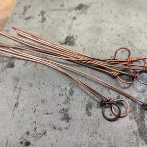 May include: A group of ten copper wire pieces with loops at the end. The wire is a reddish-brown color and the loops are a shiny gold color.