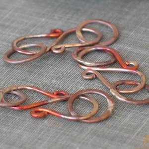 May include: Three copper wire loops with a reddish-brown patina. The loops are intertwined and have a delicate, intricate design.