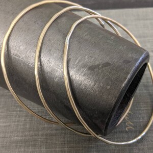 K&ouml;nnte beinhalten: Vier goldfarbene Metallarmreifen, die &uuml;bereinander gestapelt sind. Die Armreifen sind glatt und gl&auml;nzend.