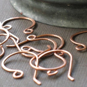 May include: A close-up of a group of copper earring hooks. The hooks are all the same size and shape, and they are arranged in a random pattern.