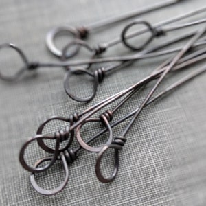 May include: A group of 10 copper wire headpins with loops at the end. The headpins are arranged in a random pattern on a textured surface.