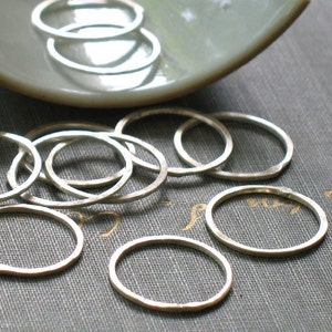 May include: A collection of silver rings, some stacked on top of each other, on a textured gray surface.