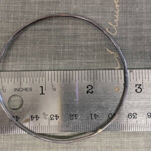 K&ouml;nnte beinhalten: Ein silberner Metallring mit einem Durchmesser von 5 cm, der zur Gr&ouml;&szlig;enbestimmung auf einem Lineal platziert ist.